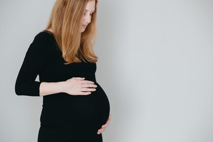 A woman with preeclampsia in a black dress, holding her pregnant belly 