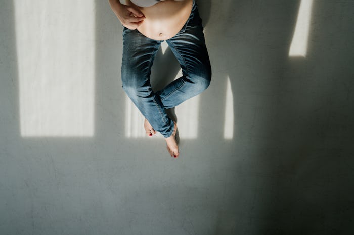A pregnant woman sitting on the floor, wondering what could help her minimize stretch marks
