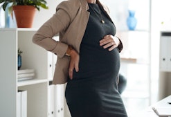 A millennial woman pregnant after doing IVF wears a black outfit at the office