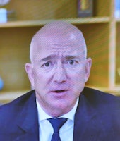 Jeff Bezos is seen in a suit and tie on a TV screen. He appears to be perspiring as his nearly hairl...