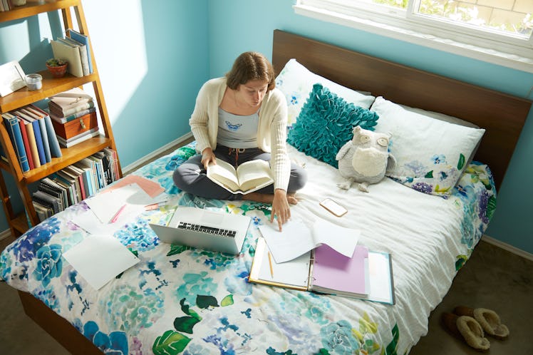 A woman studies on her bed in her college dorm room. 