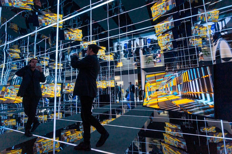 A man standing in a mirrored room of TVs.