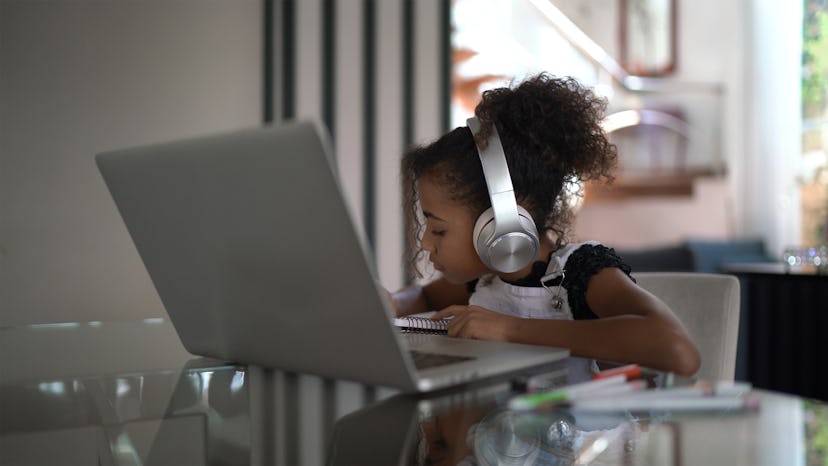 A little girl with headphones sitting in front of a laptop