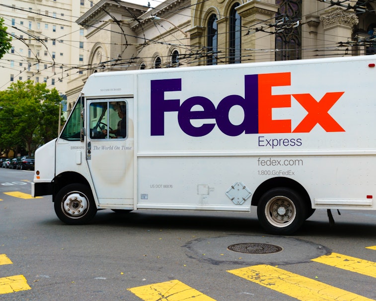 A FedEx truck with the purple and orange logo is seen on a road.