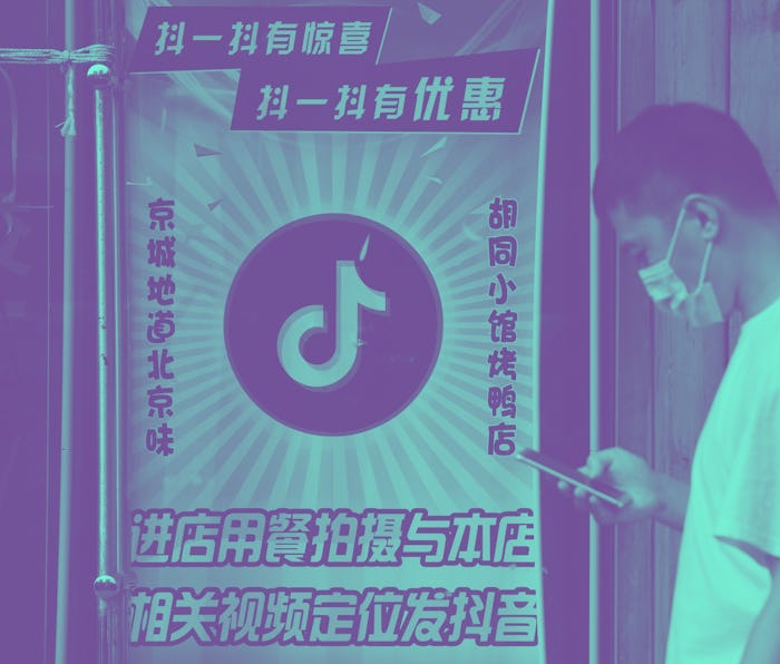 A man wearing a face mask can be seen on his smartphone while passing by a poster for TikTok.