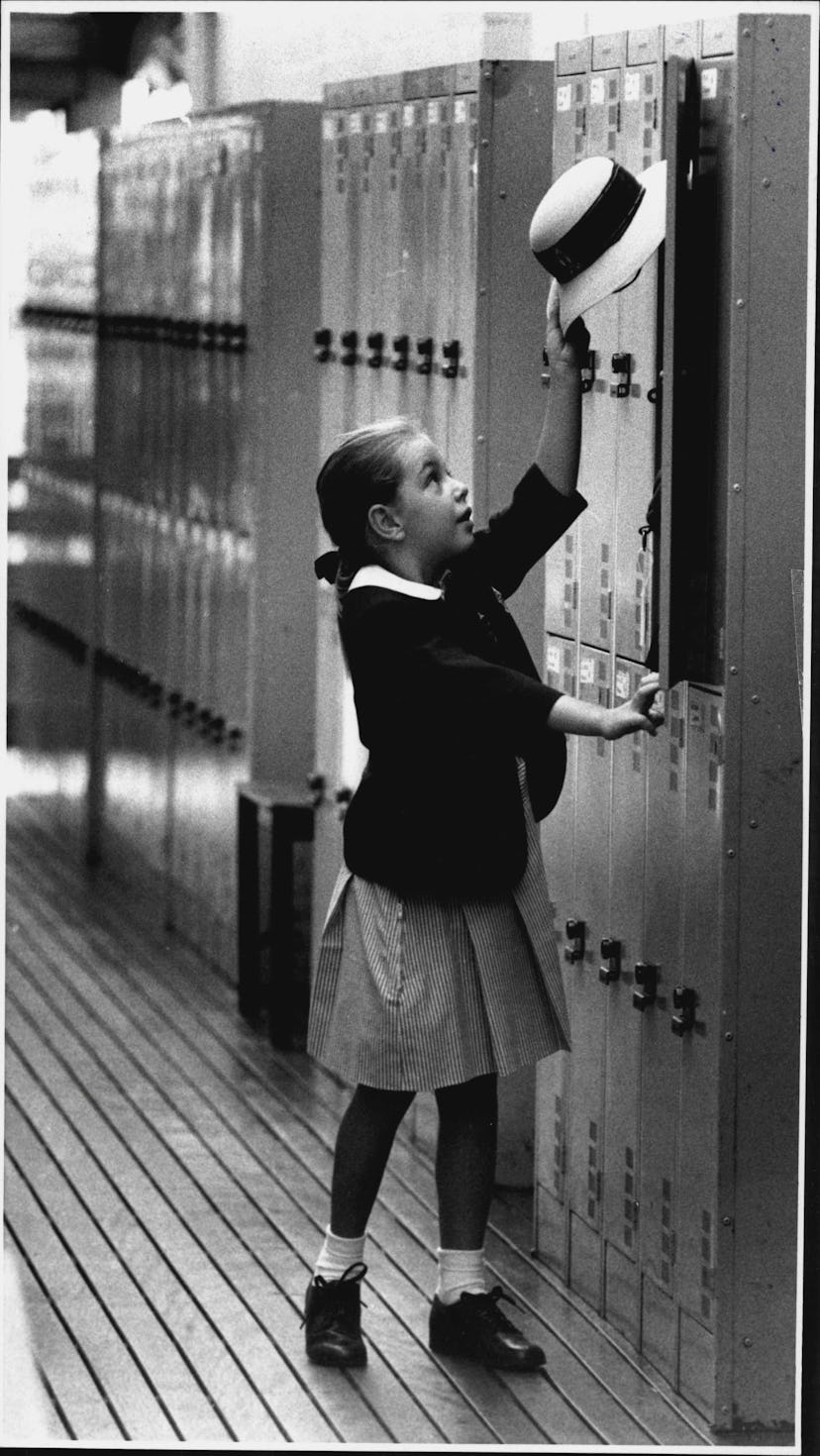 This vintage back to school photo shows a little girl attempting to put her hat in her locker. 