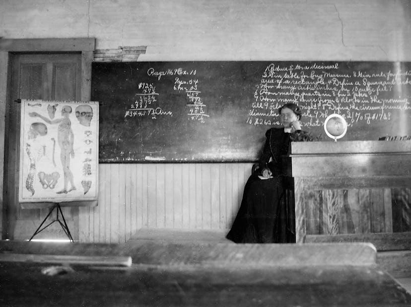 This vintage back to school photo shows a teacher in front of her chalkboard. 