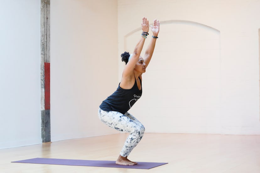 A person with natural hair and patterned yoga pants sinks into chair pose. Chair pose builds core st...