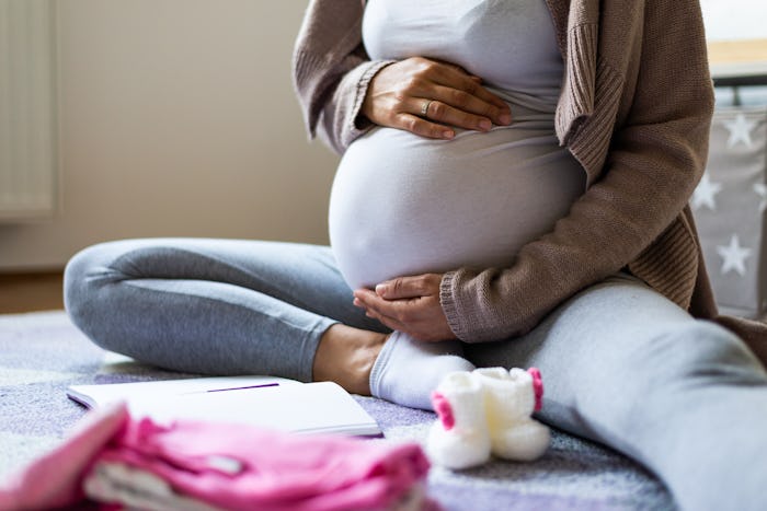 A pregnant woman with Gestational Diabetes sitting on the floor with her hands on her stomach