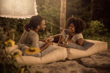 A happy couple leans on pillows and holds wine glasses in their backyard while watching a movie. 