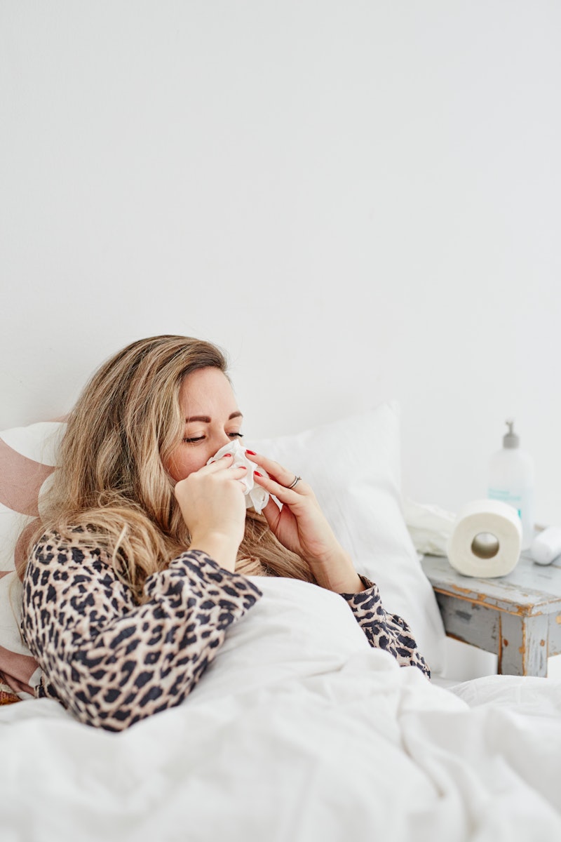 A woman blows her nose while sitting up in bed feeling sick