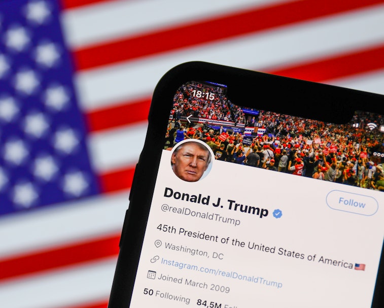 The official Twitter account for Donald Trump is seen in front of the American flag.