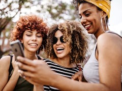 Three best friends look at a text on a phone, while laughing. 