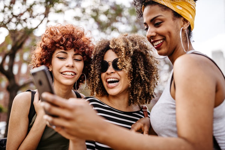 Three best friends look at a text on a phone, while laughing.