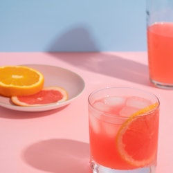 A pink grapefruit and orange cocktail against a pink and blue background. Alcohol can negatively aff...