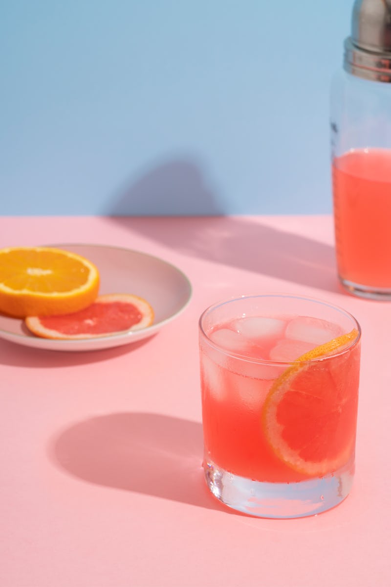 A pink grapefruit and orange cocktail against a pink and blue background. Alcohol can negatively aff...