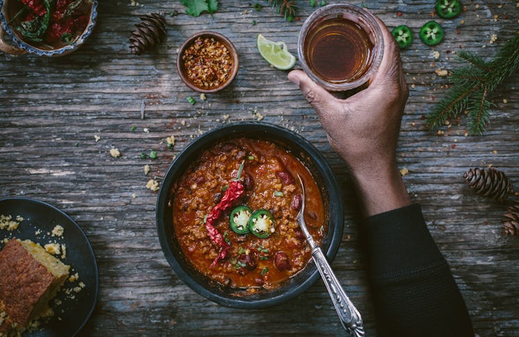 A bowl of turkey chili sits on a wooden table next to a refreshing drink.