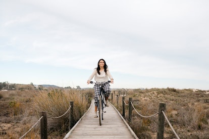 A young woman bikes down a tiny boardwalk near the beach.