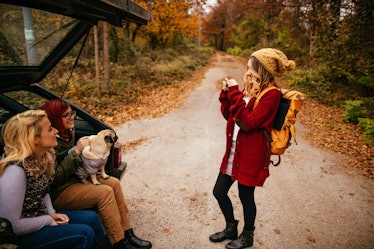 A woman takes a picture of her friends in the back of their car on a fall road trip. 