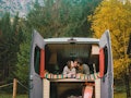 A couple kisses while getting cozy in the back of their camper van that's parked in a forest in the ...