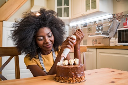 A woman frosts and decorates a chocolate cake in her kitchen, for which she'll need Instagram captio...