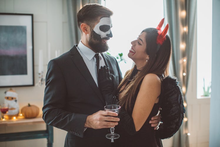 A couple dressed in Halloween costumes embrace while holding drinks. 