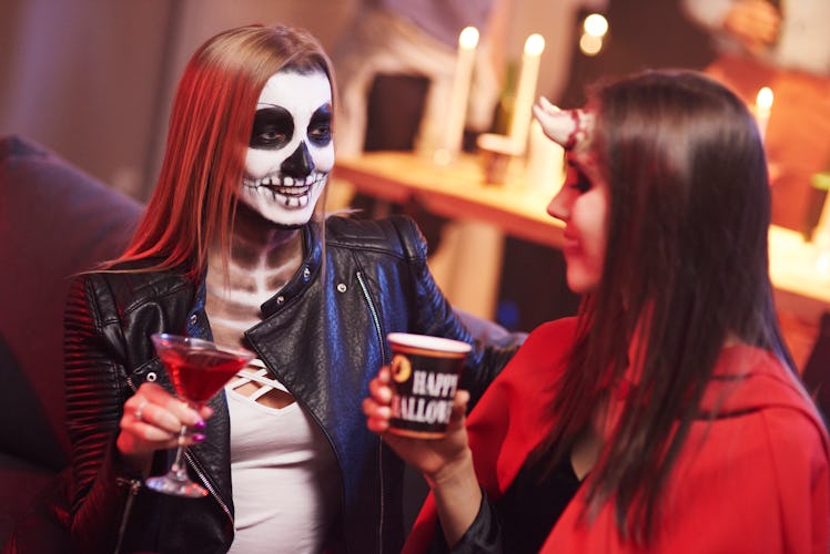 A couple dressed in Halloween costumes, sit on the couch at a party with cocktails in hand. 