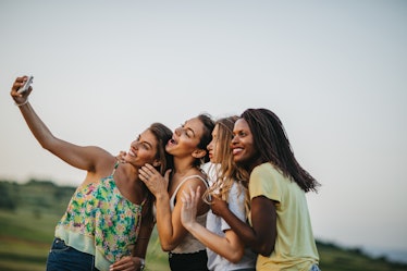 A group of women embrace while taking a selfie outside in a field.