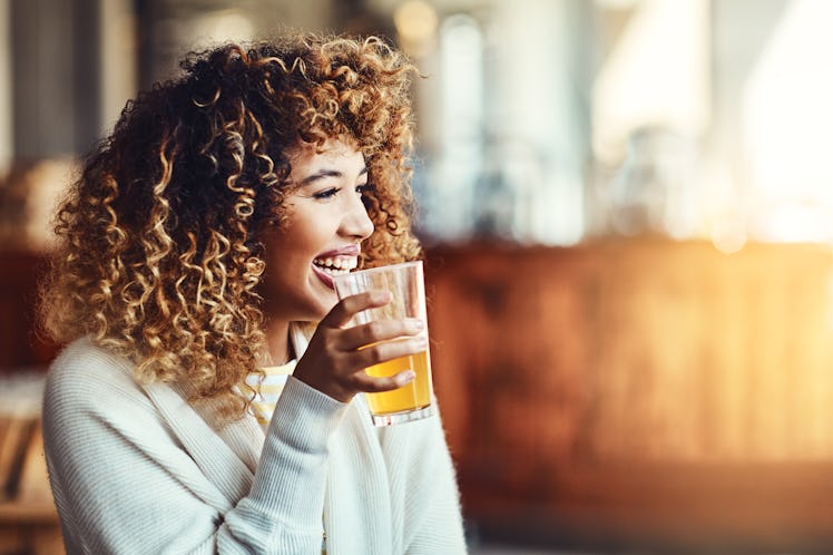 A happy woman in a sweater laughs while holding her cup of beer.