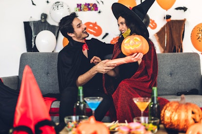 A couple dressed up for Halloween embraces on the couch with Halloween decor all around.