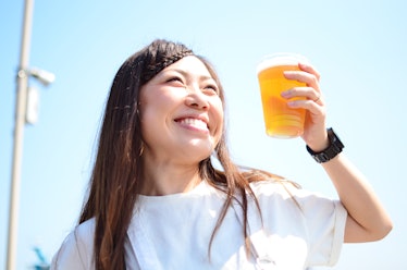 A happy woman in a white T-shirt smiles up at the sky and holds a cup of beer.