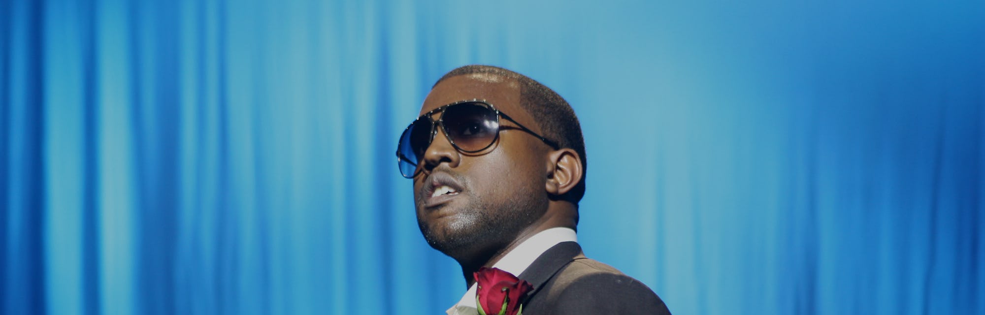 Rapper and artist Kanye West can be seen in a suit with a red handkerchief in his pocket. He is wear...