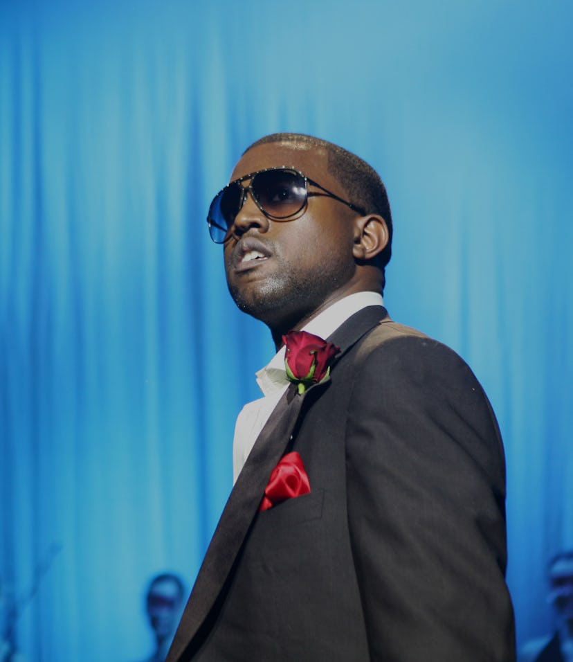 Rapper and artist Kanye West can be seen in a suit with a red handkerchief in his pocket. He is wear...