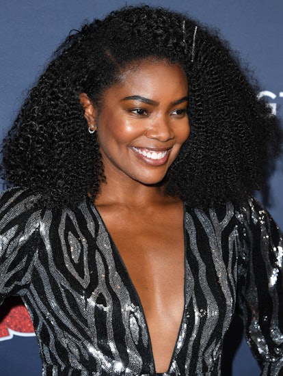 Gabrielle Union smiling on a red carpet event in a deep V-neck dress in black-and-white with sequins...