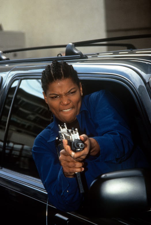 Queen Latifah, holding a gung while leaning out of a car window 