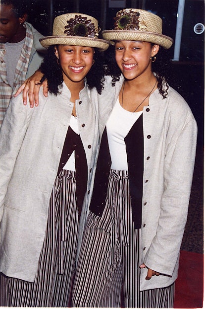 Tia and Tamera in white tops, black sweaters, grey jackets, black-white striped pants and beige hats