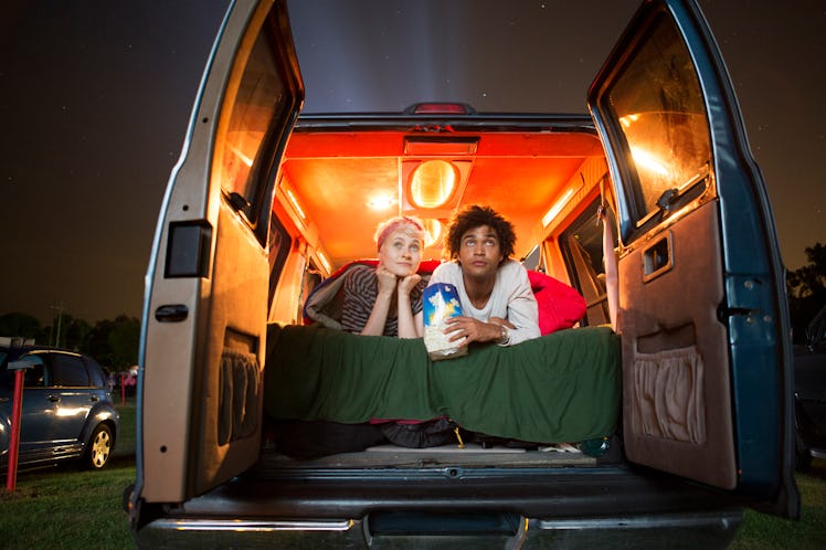 A young couple sits in the trunk of their car and watches a movie at a drive-in.