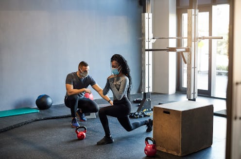 A woman works out with a trainer, both wearing masks. Returning to the gym during COVID feels weirdl...