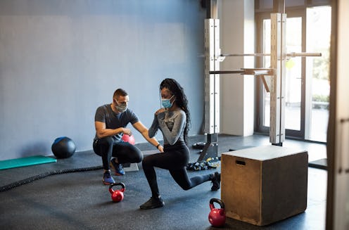 A woman works out with a trainer, both wearing masks. Returning to the gym during COVID feels weirdl...