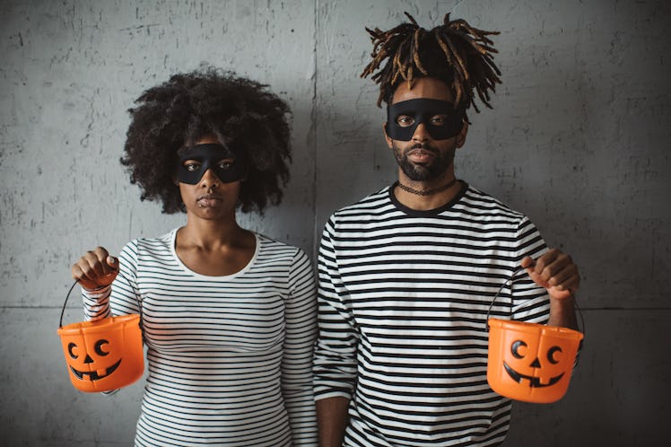 A young couple looks seriously at the camera while holding plastic pumpkin baskets.