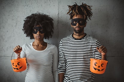A young couple looks seriously at the camera while holding plastic pumpkin baskets.