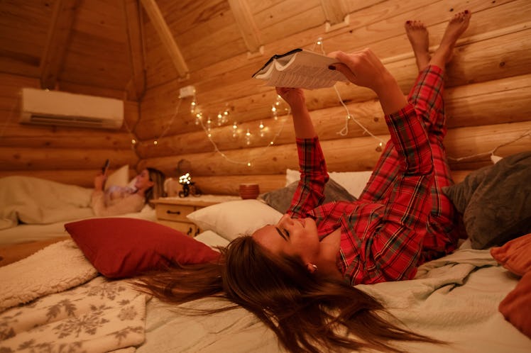A woman in flannel PJs reads in bed in her cozy cabin room.