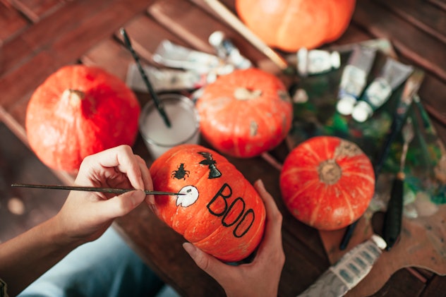 Person decorating small pumpkins by painting on them.