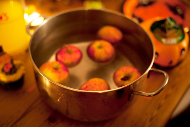Apples in a pot of water on a table with halloween decorations.