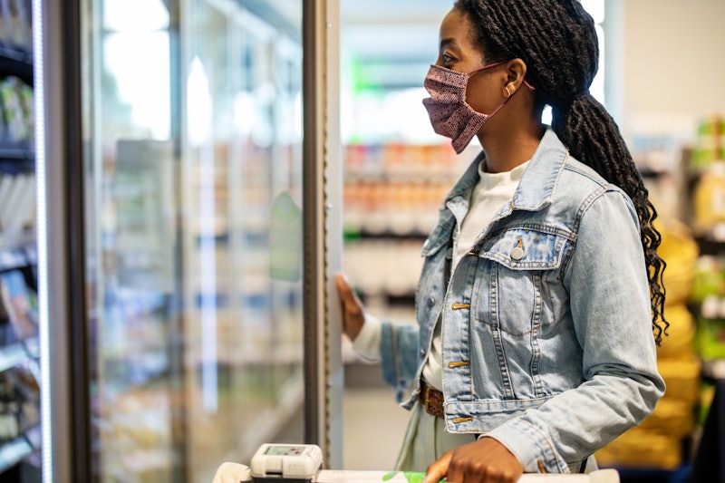 A woman wearing a jacket and mask opens a fridge door at a grocery store. Doctors explain how the se...