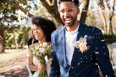 A young Black couple smile while walking through confetti after getting married in their backyard.