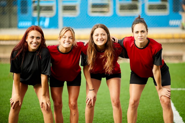 A group of women wearing sports uniforms stand together on the field. 