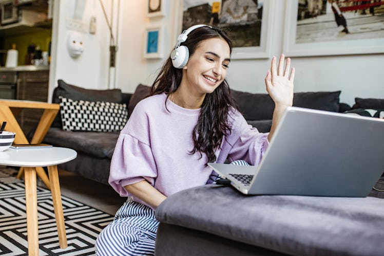 A young woman waves at her laptop while FaceTiming with her long-distance best friend.