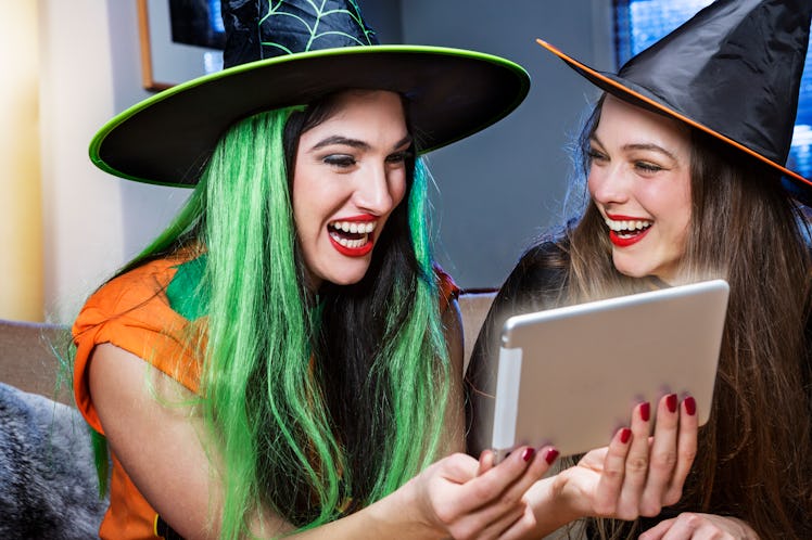 Friends dressed like witches on Halloween look at a tablet. 