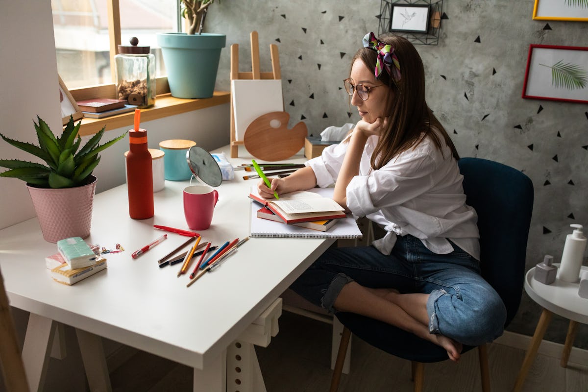A girl sits crossed legged at her desk, studying a book.